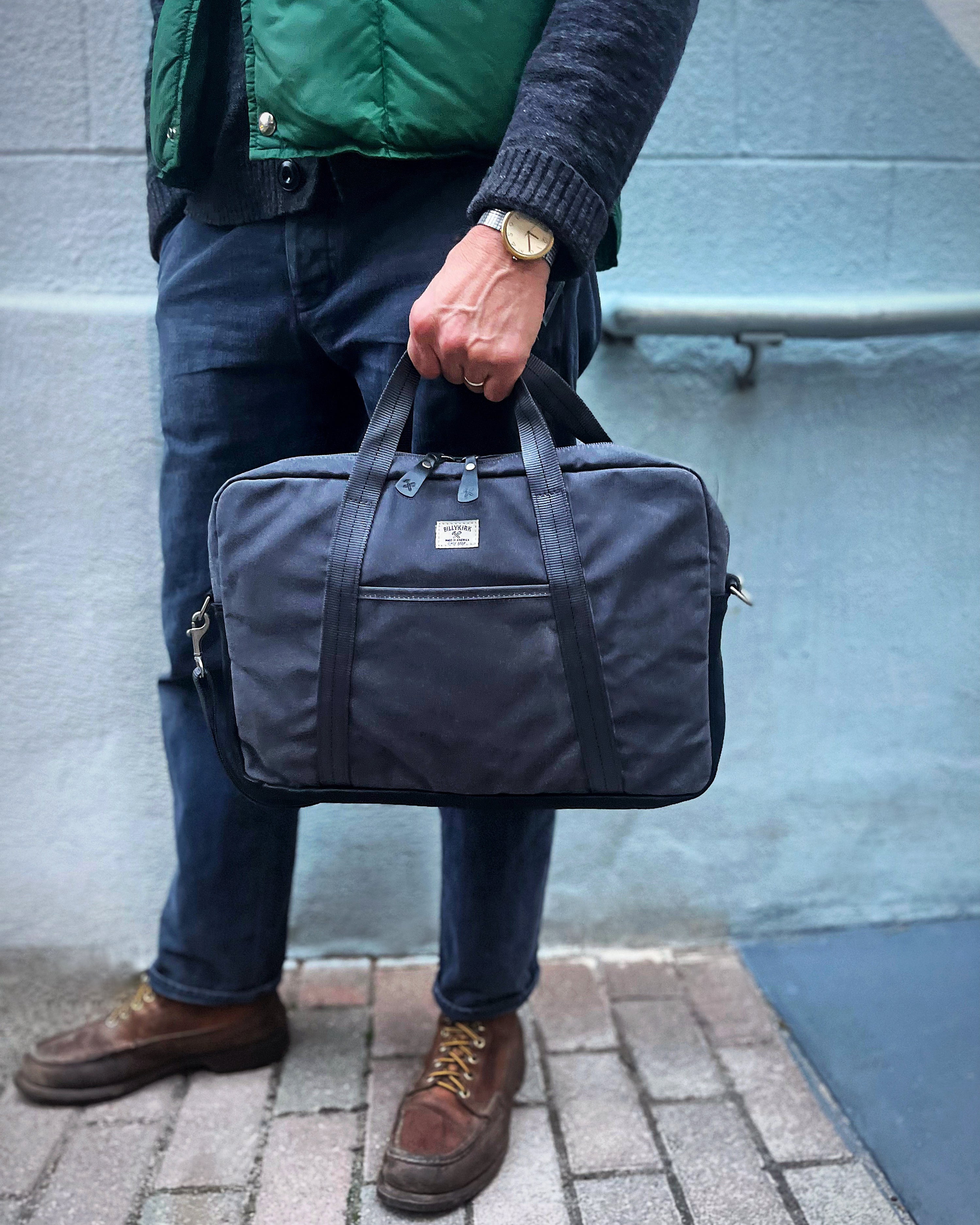 A gray fabric laptop bag with a zipper closure, two short carrying handles, an adjustable shoulder strap, and a small white label on the front. The bag is photographed against a plain white background.