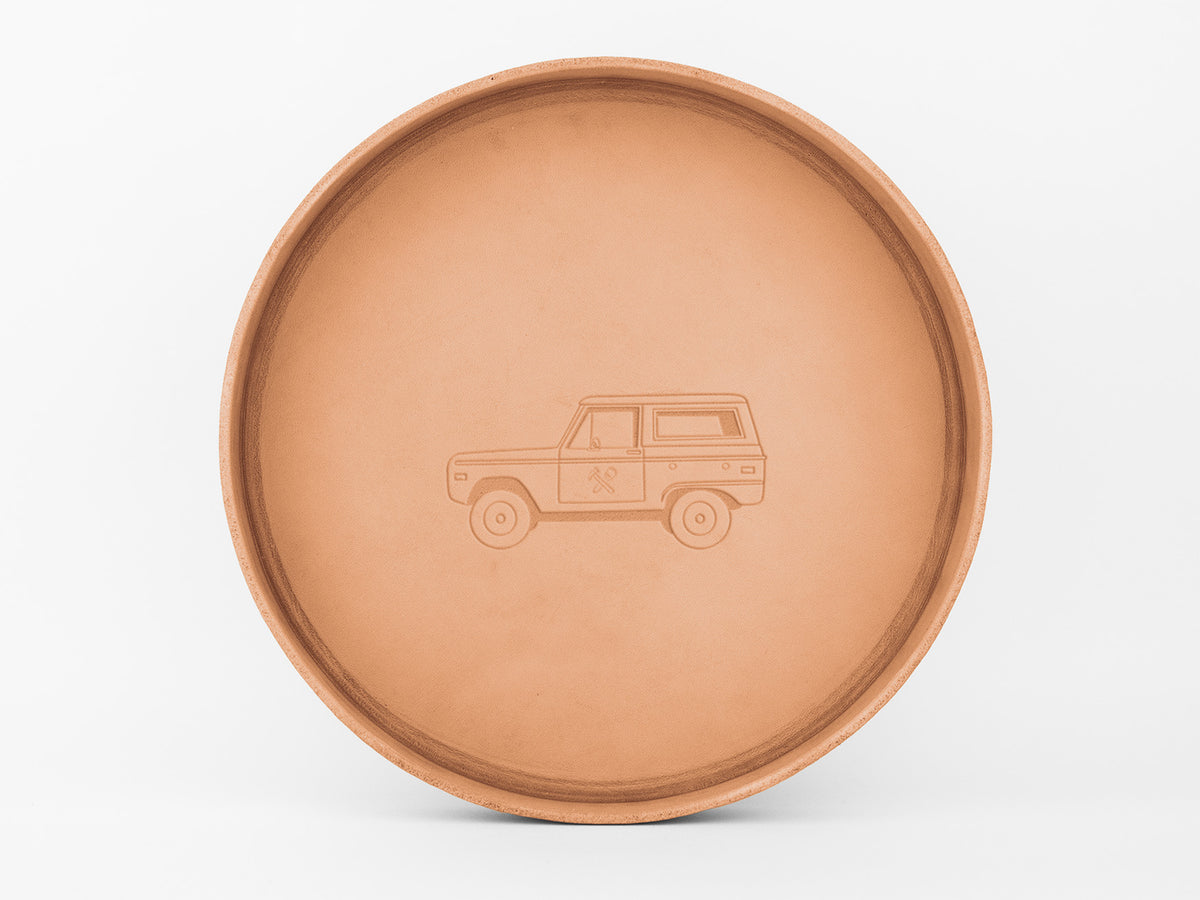 A round, light brown tray with an embossed outline of a vintage SUV and two crossed paddles on its side, centered on a plain white background.