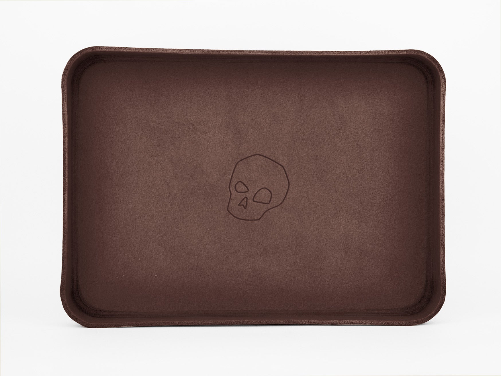 A rectangular brown tray with raised edges features a simple, outlined skull design engraved in the center. The background is white.