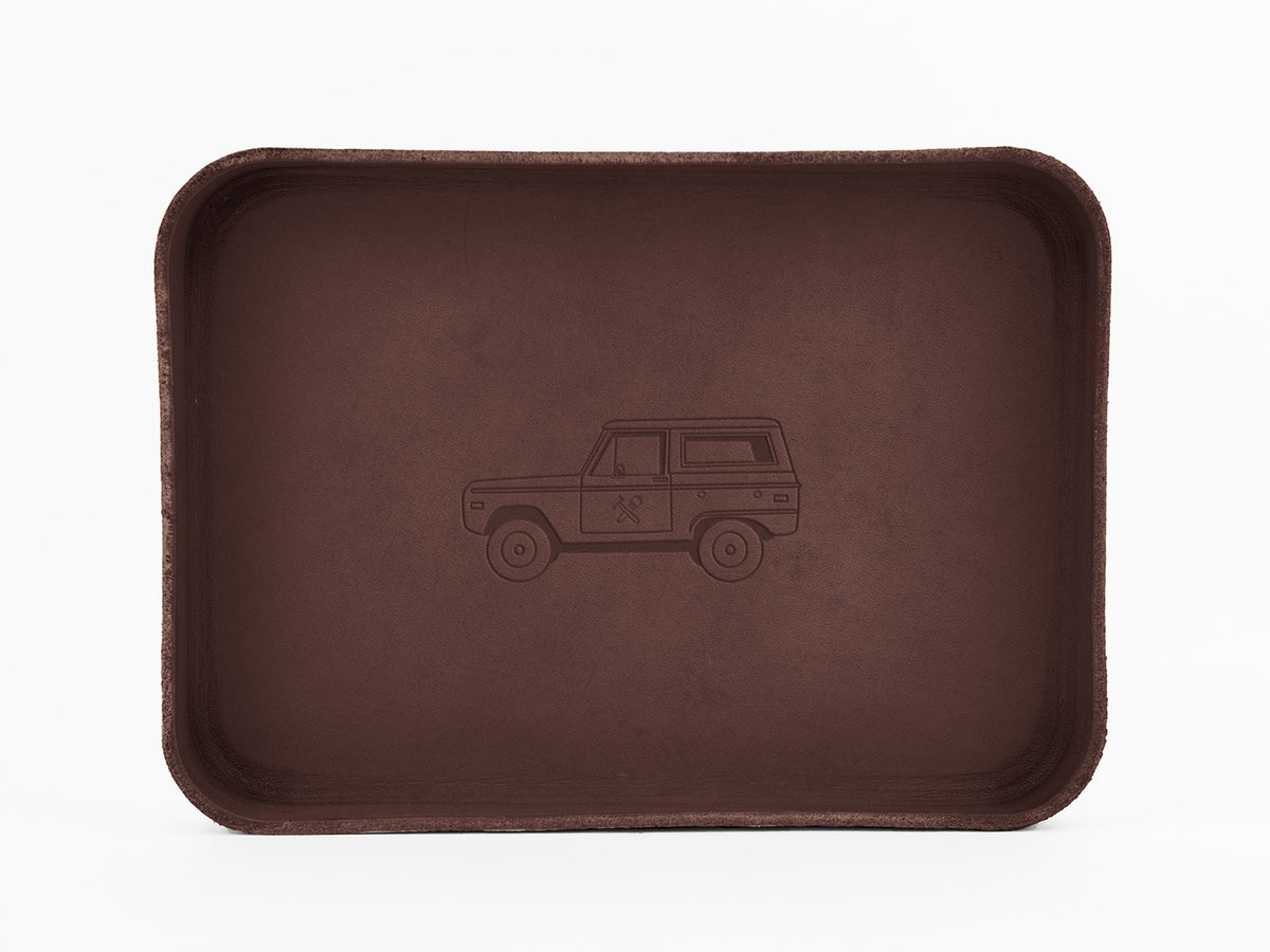 A rectangular brown tray with rounded corners features an outline drawing of a vintage SUV engraved in the center. The background is plain white.