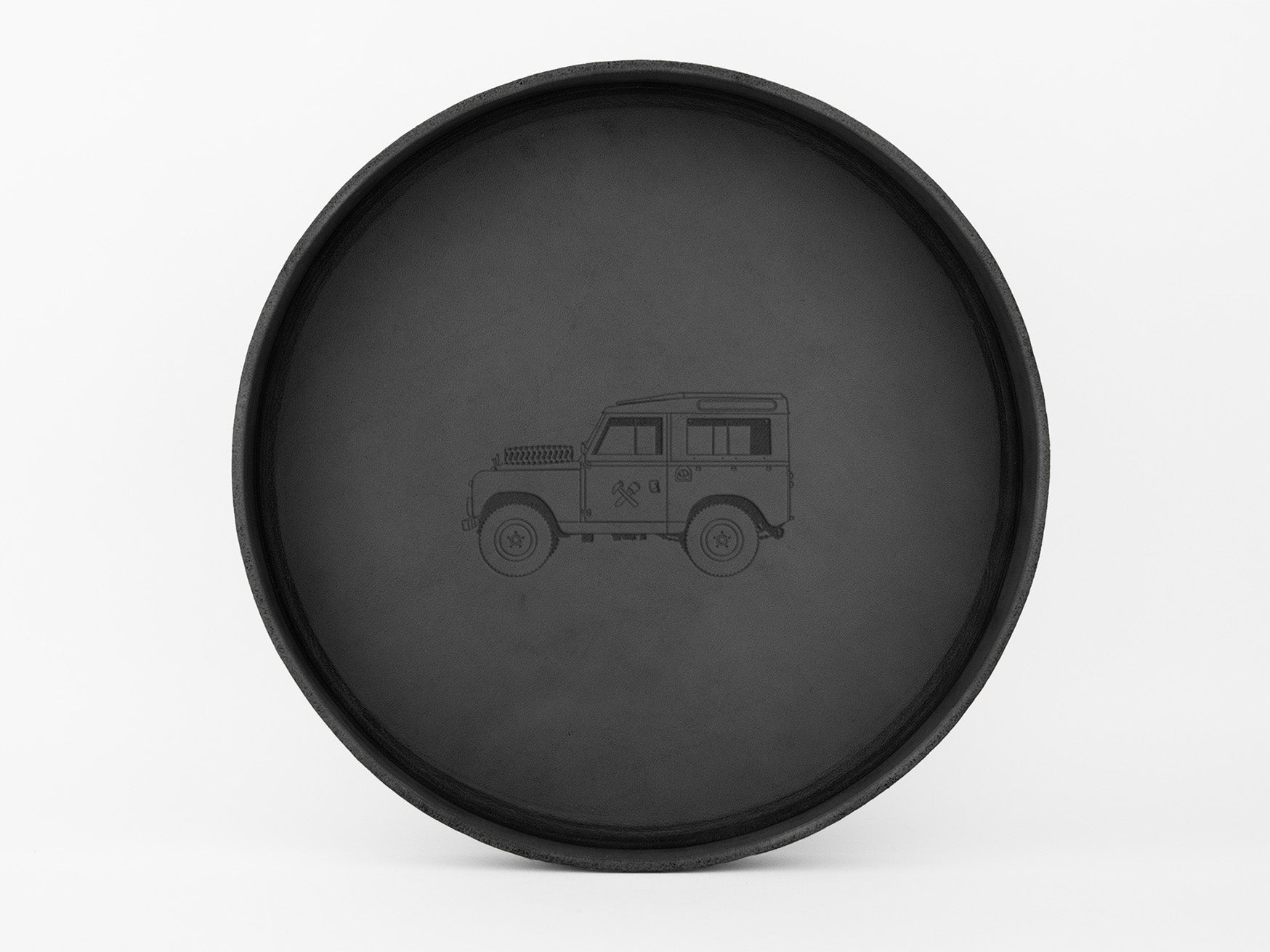 A round, black tray with a simple outline drawing of a classic off-road vehicle, viewed from the side, in the center against a plain white background.