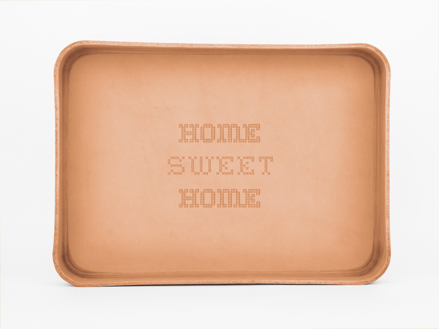 A rectangular, tan leather tray with the words HOME SWEET HOME embossed in a stitched-style font in the center. The background is plain white.