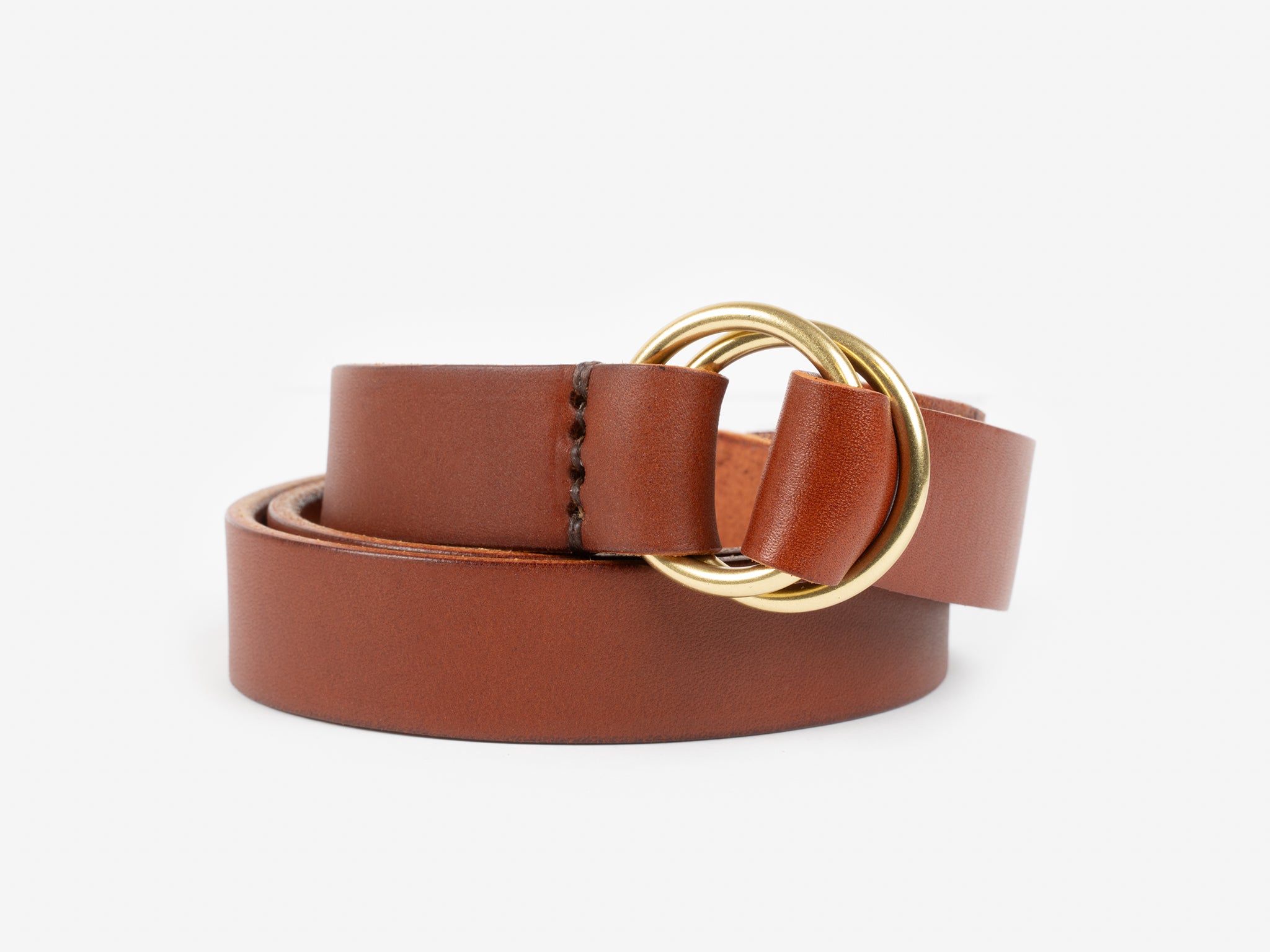 A tan leather belt with a double round gold rings, coiled neatly on a plain white background.