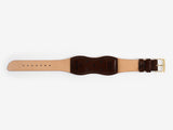 The back of a dark brown cordovan leather watch strap with a brass buckle lies flat on a white background; it has brown thread stitched edges and an hourglass shape.
