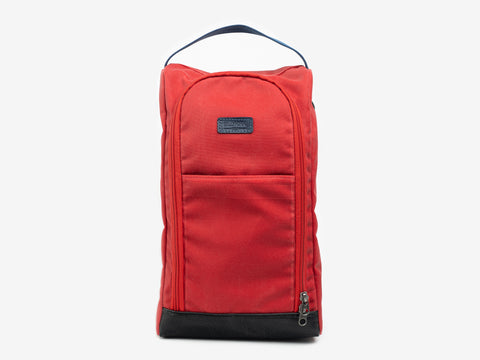 A red fabric shoe bag with a black handle on top, a front zipper pocket, and a black base, displayed against a plain light background.