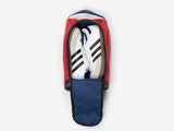 A pair of white sneakers with black stripes placed inside a red shoe bag with a navy blue interior and the top flap partially unzipped.