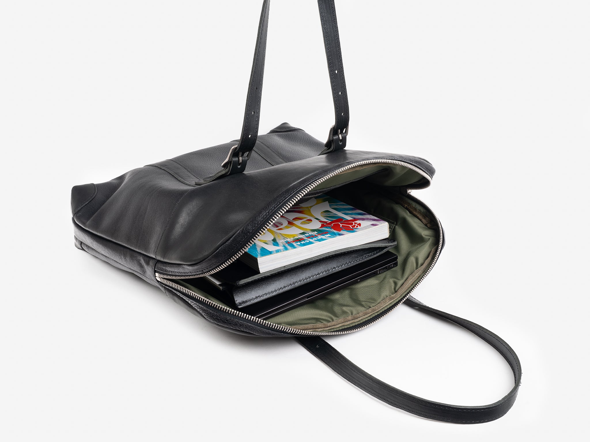 A black leather tote bag with two straps, unzipped to reveal books, a notebook, and a tablet inside, photographed on a white background.