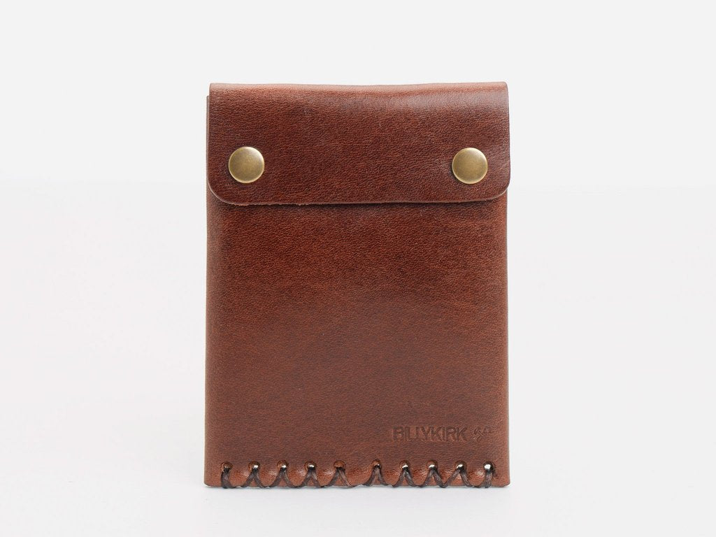 A brown leather wallet with a stitched bottom edge and two brass snap buttons on the flap, standing upright against a plain white background.
