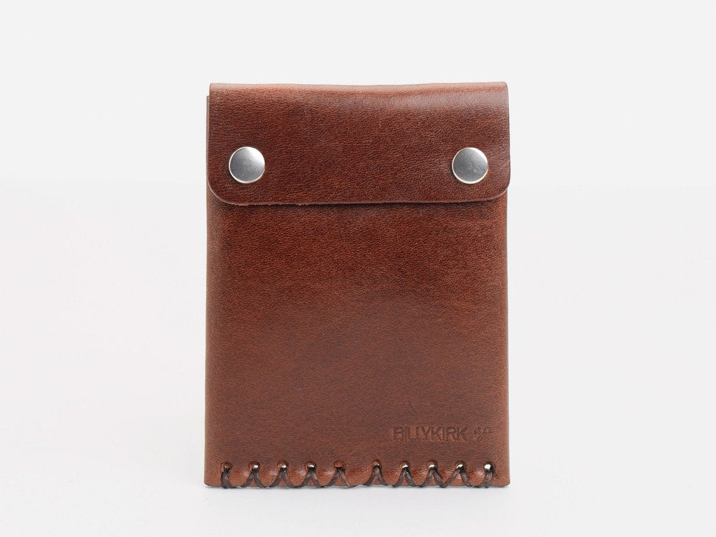 A brown leather wallet with a stitched bottom edge and two brass snap buttons on the flap, standing upright against a plain white background.