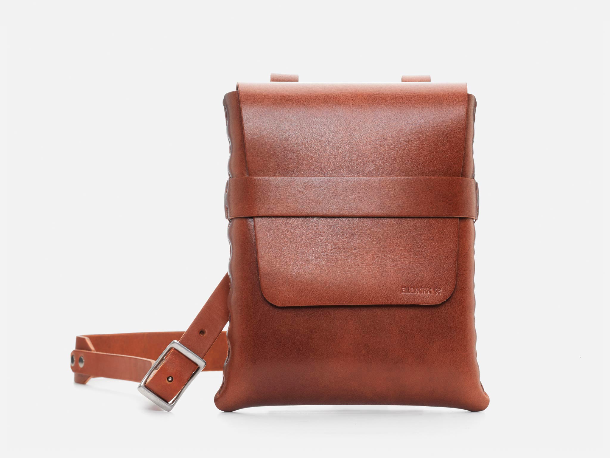A sleek, light brown leather crossbody bag with a front flap, minimalist design, and an adjustable strap with a silver buckle, displayed against a plain white background.