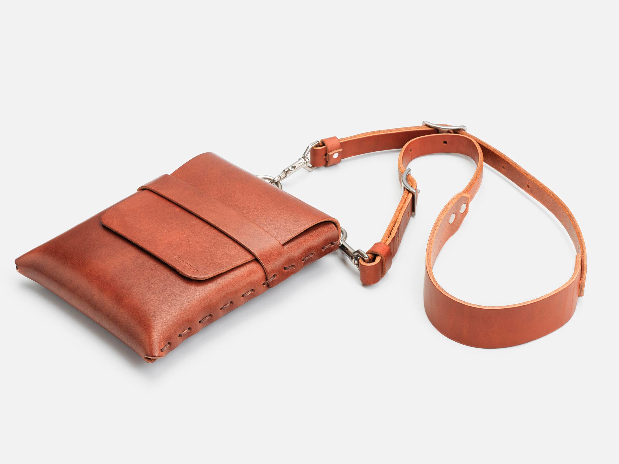A brown leather crossbody bag with a front pocket, silver hardware, and an adjustable strap, displayed on a white background.