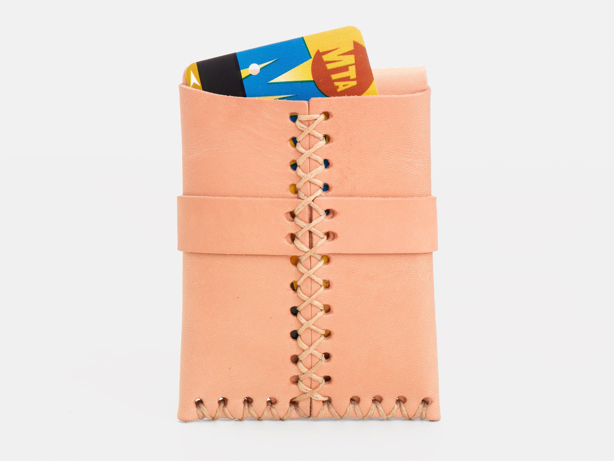 A natural colored leather wallet with visible stitching holds a New York City MetroCard,  partially sticking out of the rear wallet on a white background.