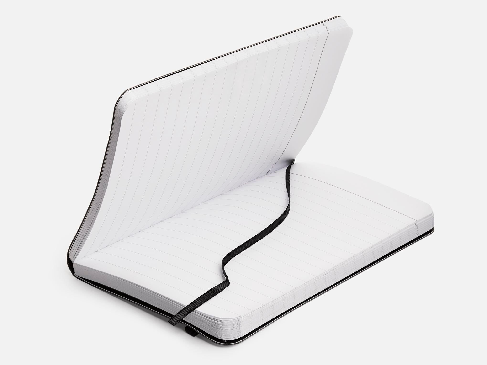 An open, lined notebook with a black cover and a black elastic strap lying across its pages, set against a plain white background.