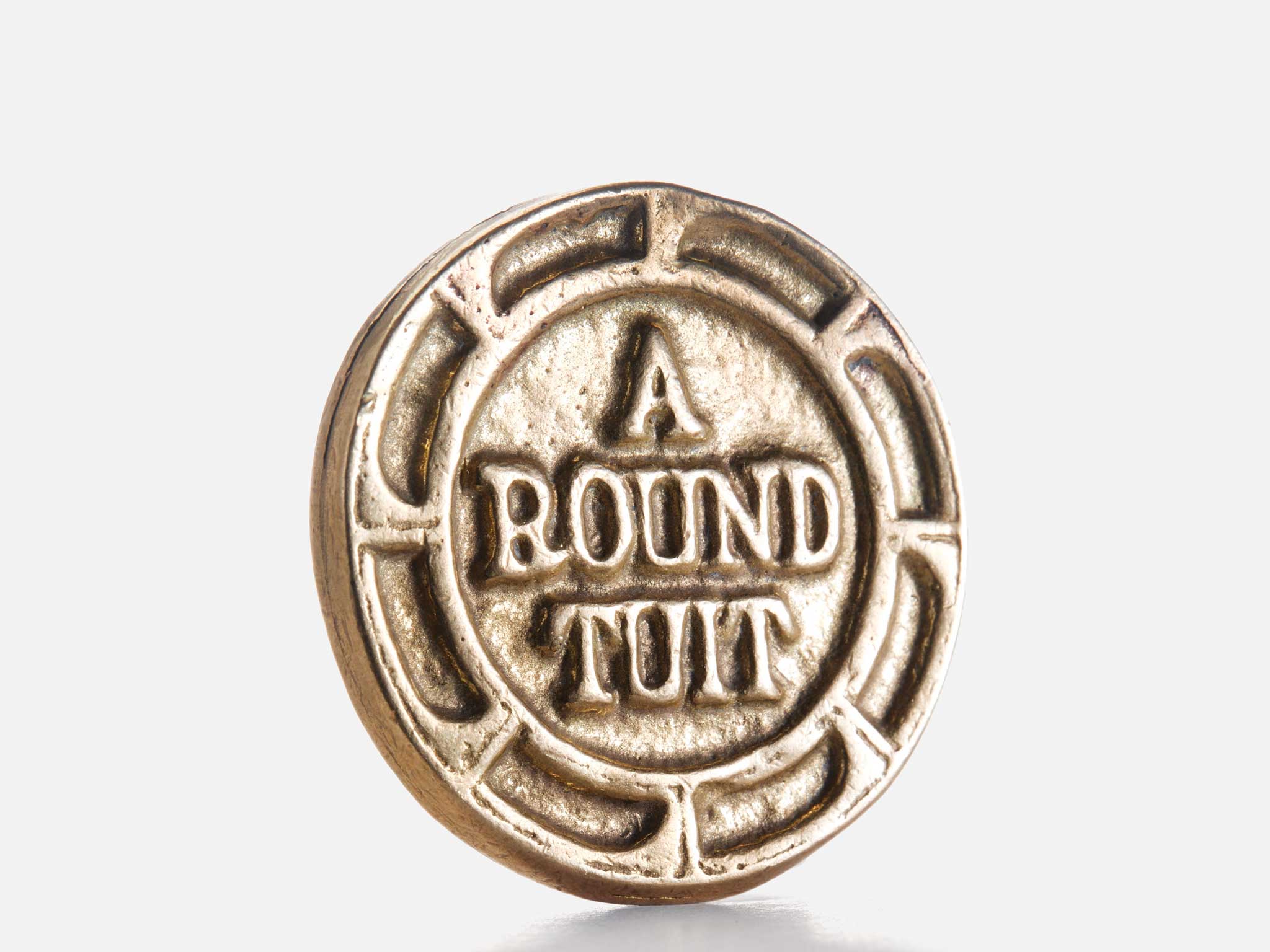A round, gold-colored coin with the words A ROUND TUIT engraved on it, resting upright against a plain white background.