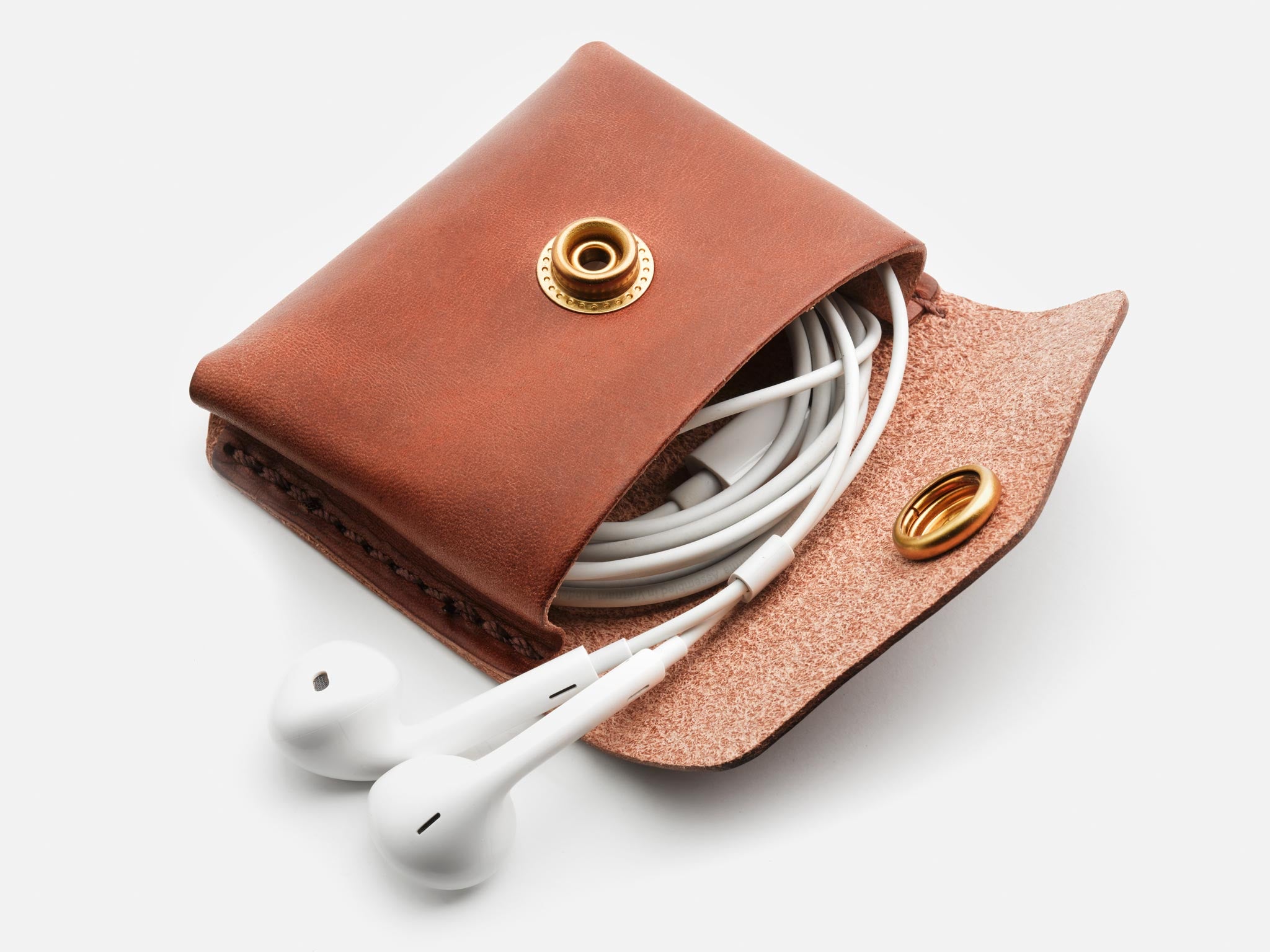A brown leather coin pouch open, displaying white earphones and a key inside, with a gold-colored snap closure.