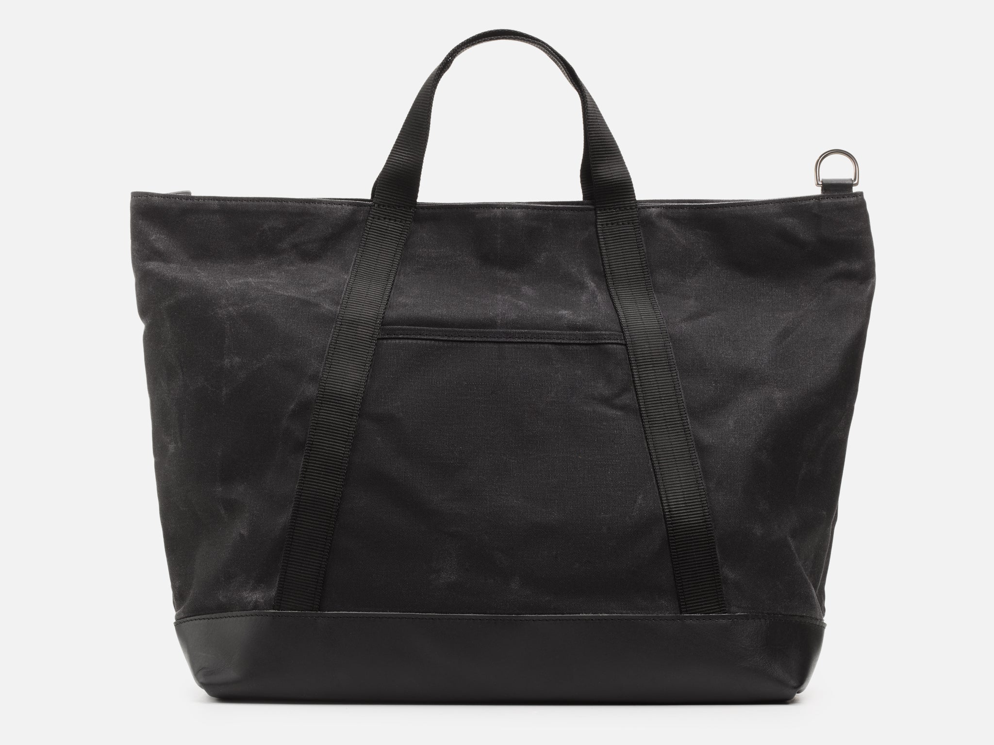 A back view of an black waxed canvas tote bag with 1" nylon black handles with pocket between the handles, and a black leather bottom, set against a plain white background.