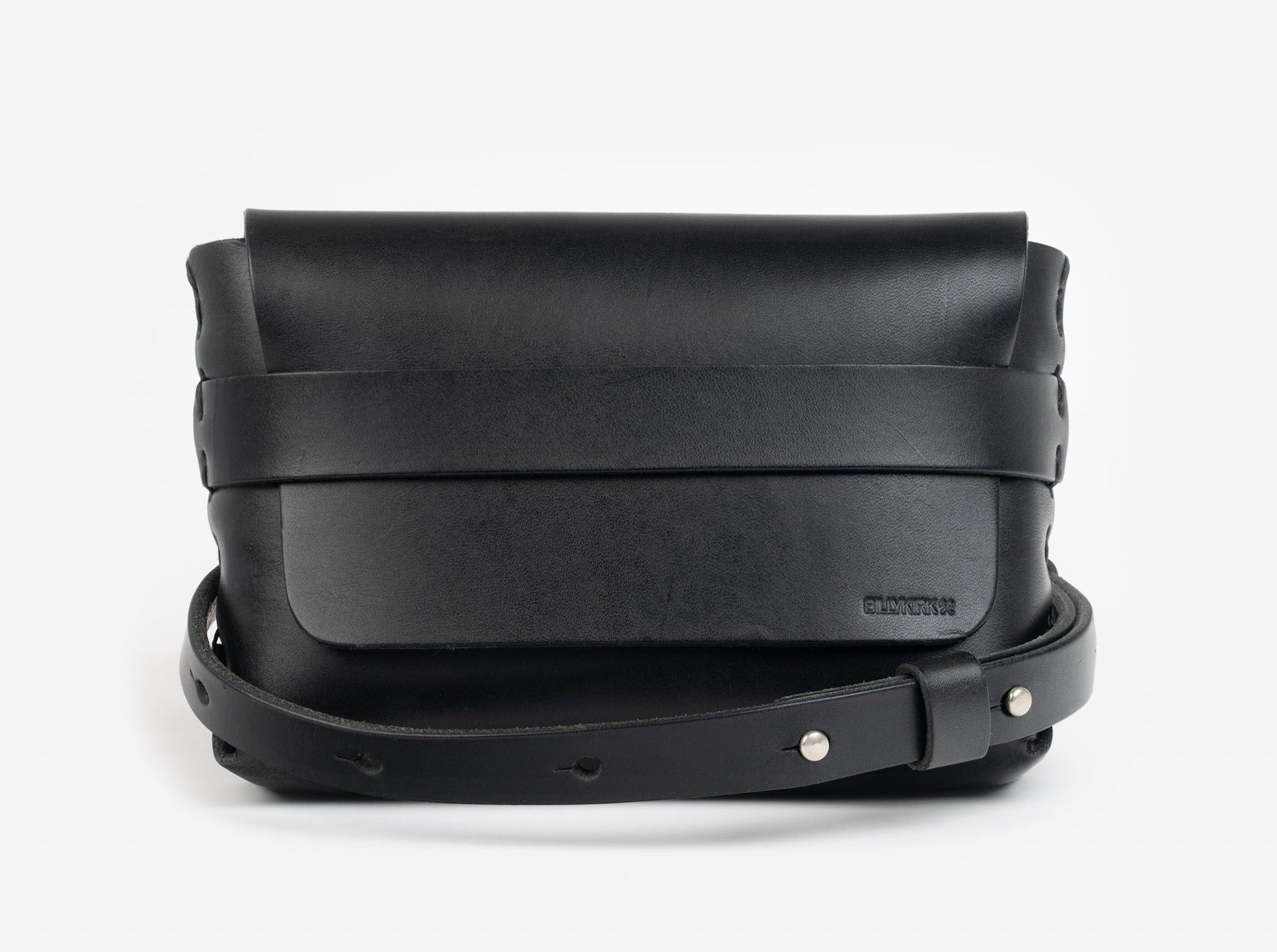 A black leather belt crossbody bag with a smooth finish, featuring a flap closure, subtle embossed branding, and an adjustable strap with silver-tone collar buttons, displayed against a white background.