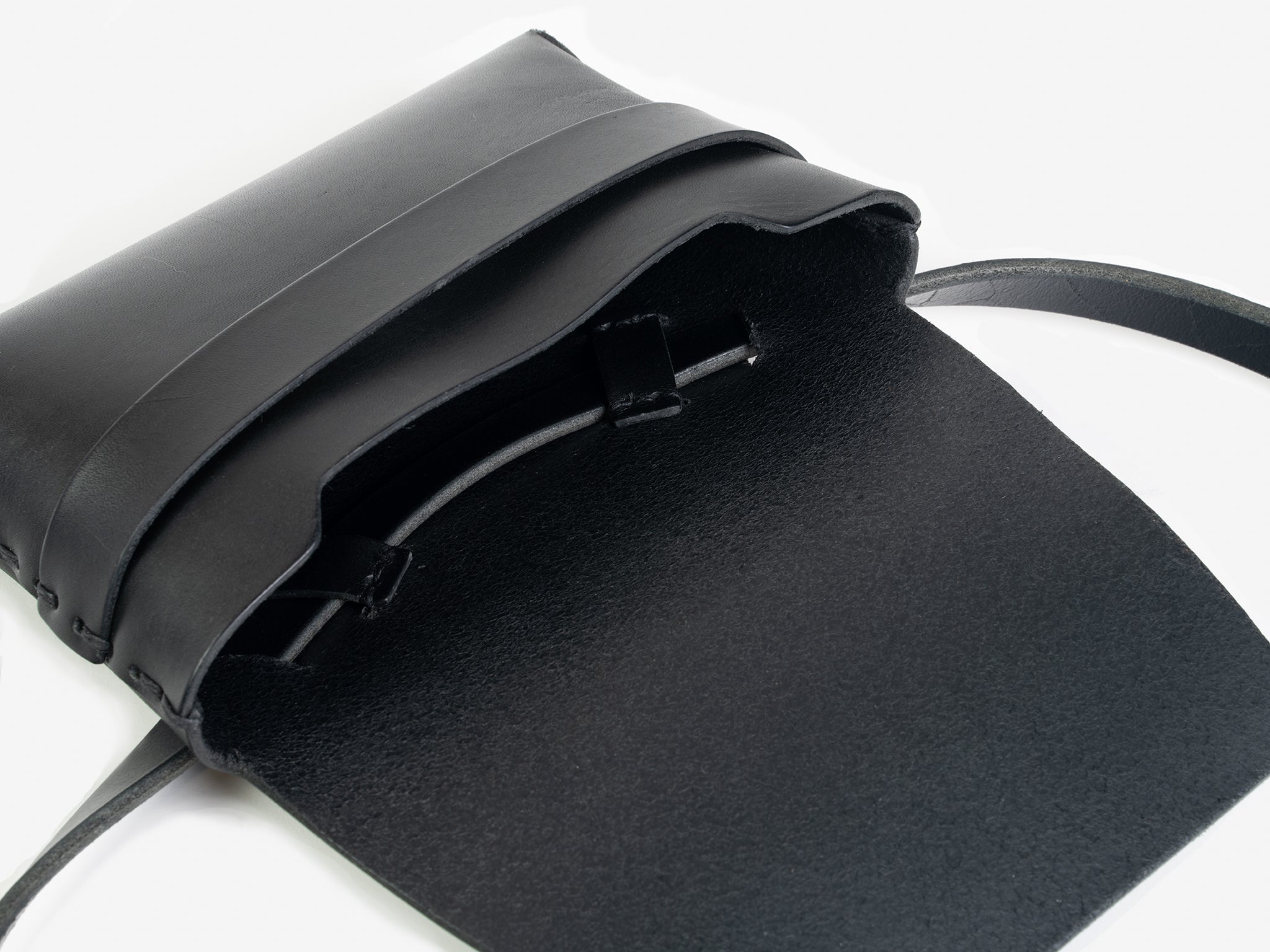 A black leather crossbody bag with a flap open, revealing some hand-stitched details. The bag has a strap and minimalist design, displayed on a white background.