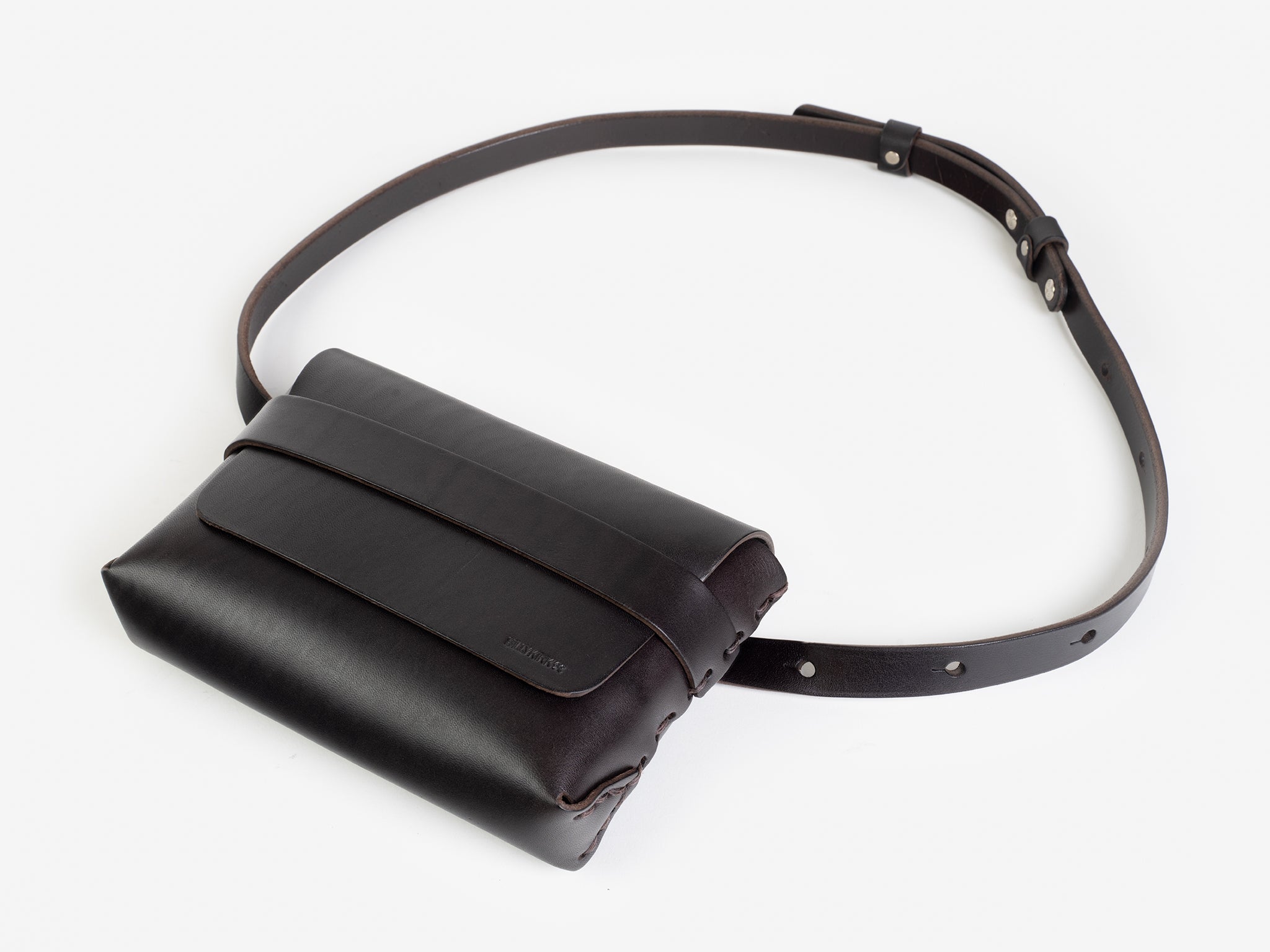 A dark brown leather belt crossbody bag with a smooth finish, featuring a flap closure, subtle embossed branding, and an adjustable strap with silver-tone collar buttons, displayed against a white background.