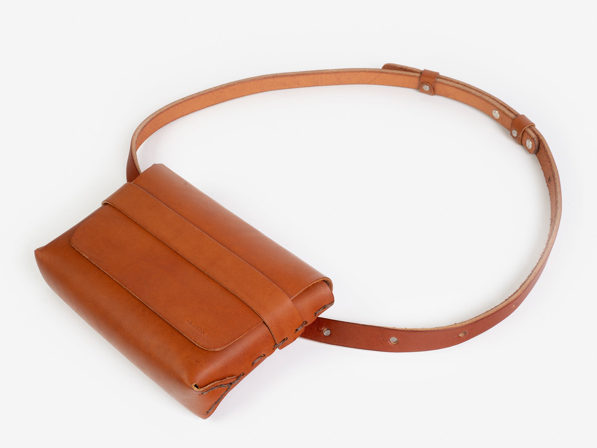 A tan leather belt crossbody bag with a smooth finish, featuring a flap closure, subtle embossed branding, and an adjustable strap with silver-tone collar buttons, displayed against a white background.