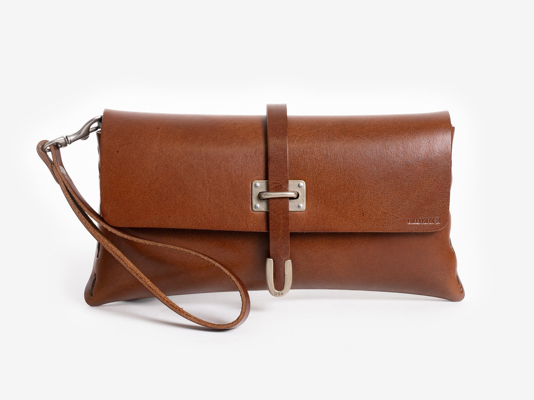 A brown leather clutch bag with a wrist strap, silver hardware, and a rectangular metal buckle on the front flap. The bag is set against a plain white background.