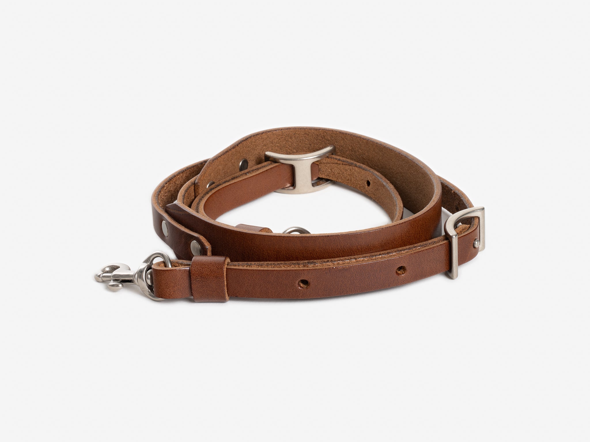 A rolled-up brown leather dog leash with metal hardware, including a buckle, clasp, and D-ring, displayed on a white background.