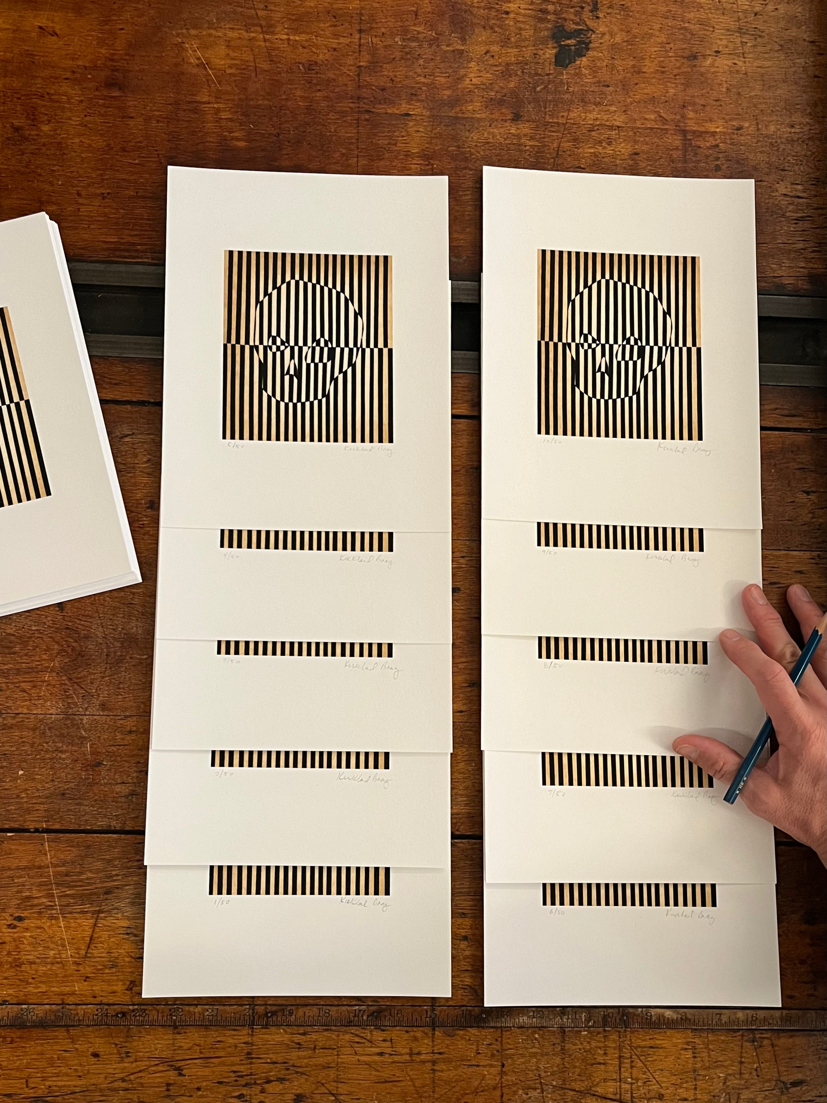 Ten Skully collages on a wooden table with a hand holding a pencil