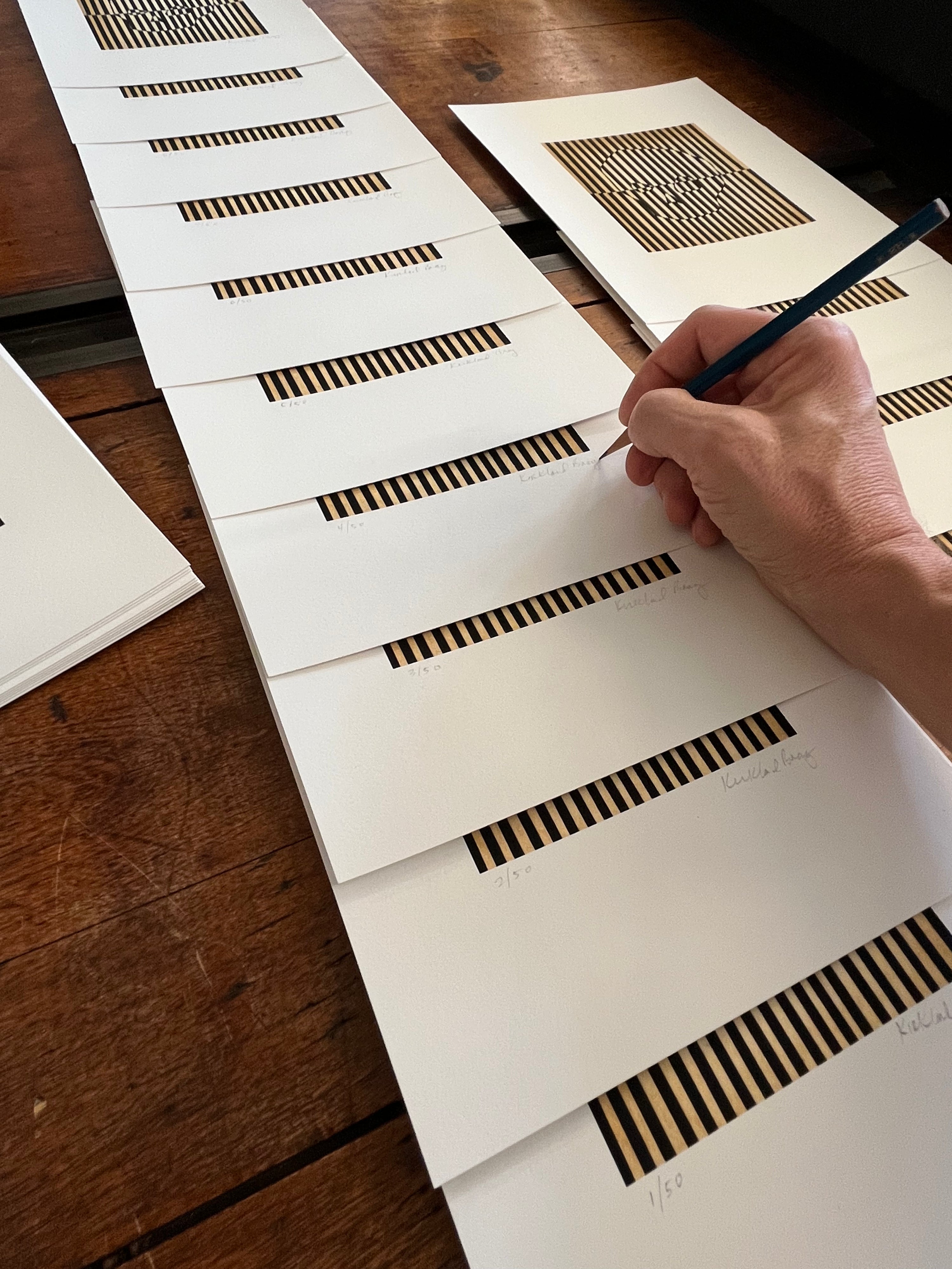 The artist's hand signing copies of the Skully collage on a wooden table