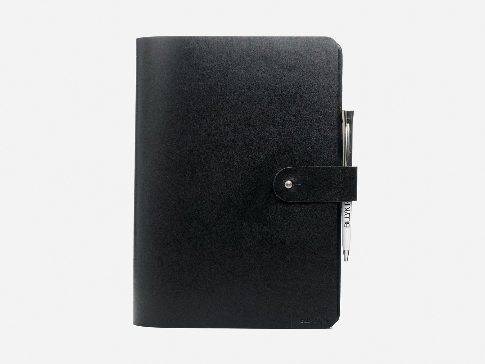 A closed black leather notebook with a snap button strap, featuring a silver pen clipped to the strap, set against a plain white background.