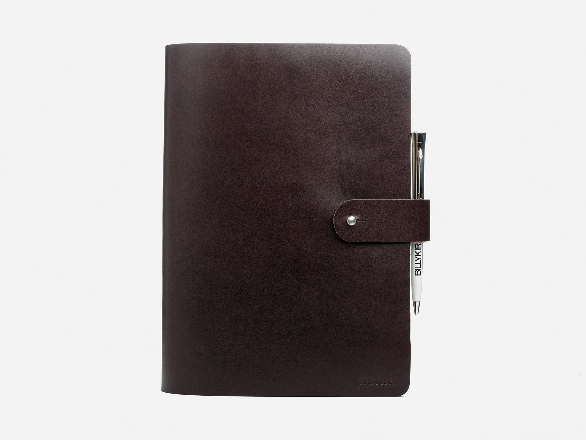 A closed, dark brown leather notebook with a snap button closure and a silver pen tucked into the side pen loop, set against a plain white background.