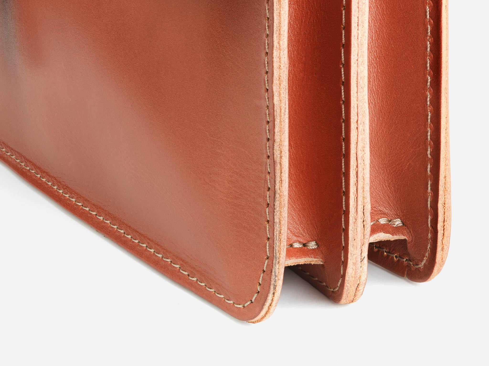 Close-up of the corner of a brown leather wallet with visible stitching and two compartments, showing smooth, polished surface and natural edges.