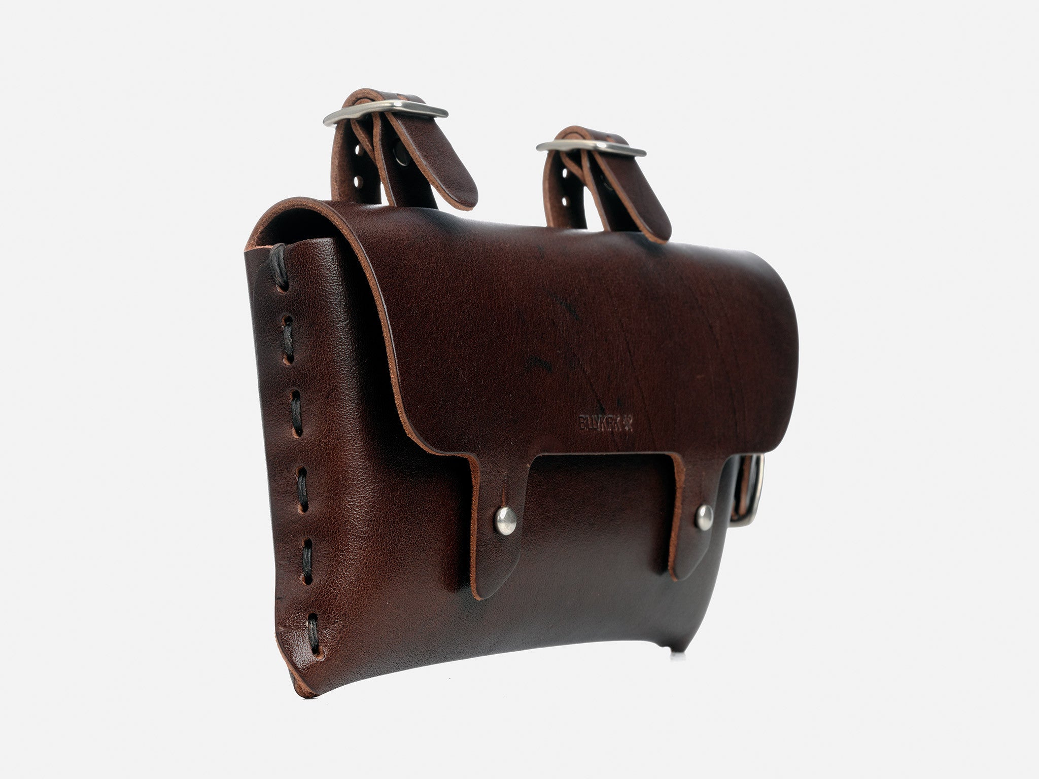 A brown leather saddlebag with two buckle straps on top and side stitching, designed for attachment to a bicycle frame. The leather has a smooth finish and metal rivets for reinforcement.