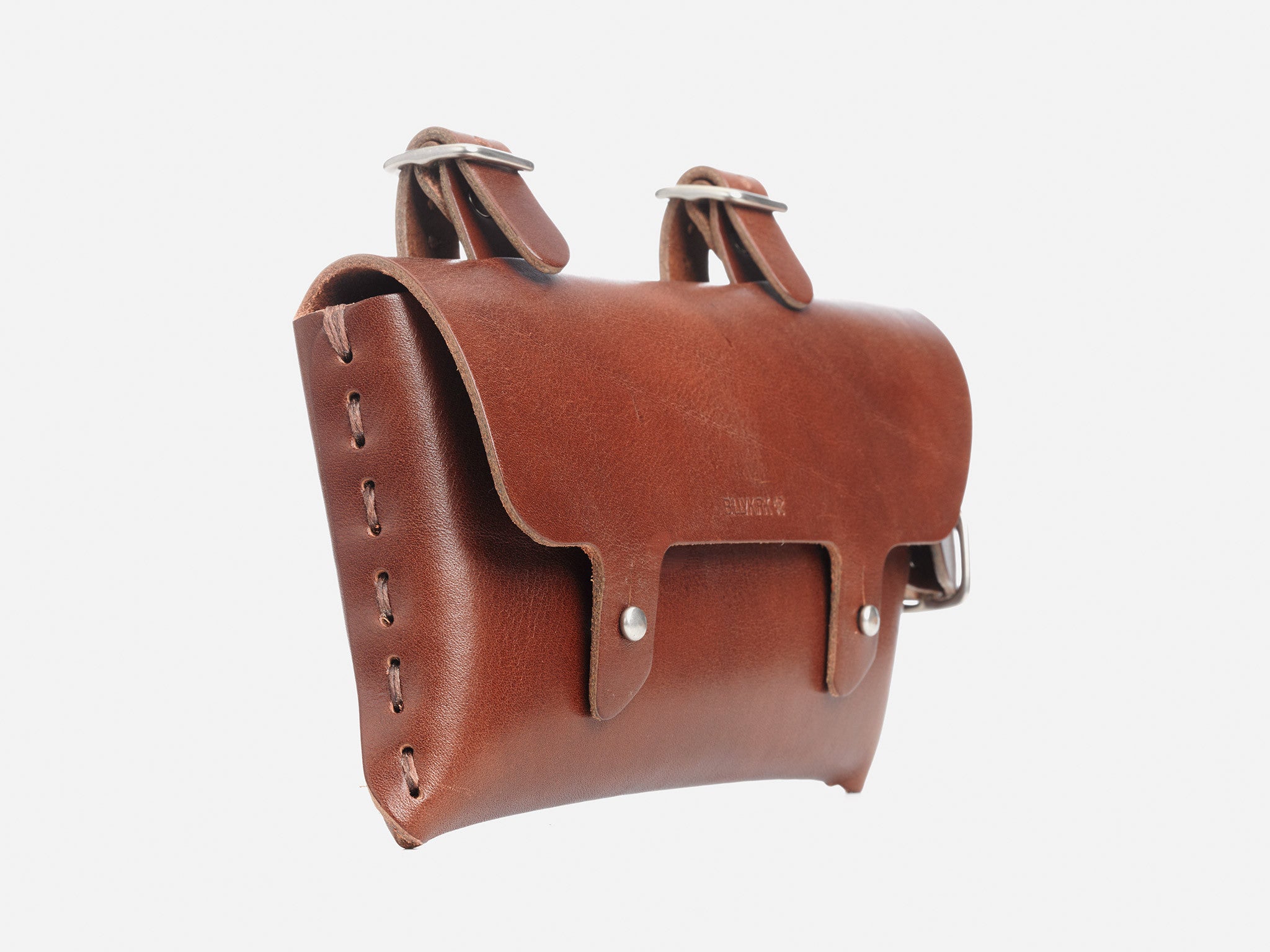 A brown leather pouch with stitched edges, a fold-over flap, and two metal buckle straps on top, photographed against a plain white background.