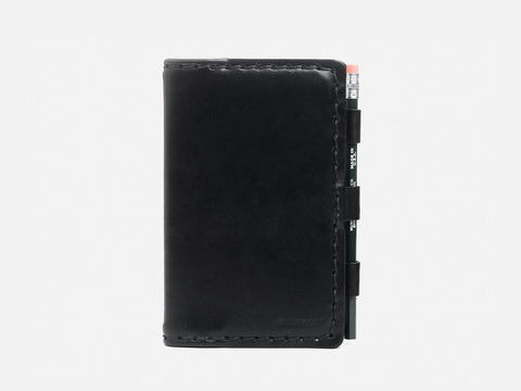 A black leather notebook cover with a pencil held in a side loop, shown against a plain white background.