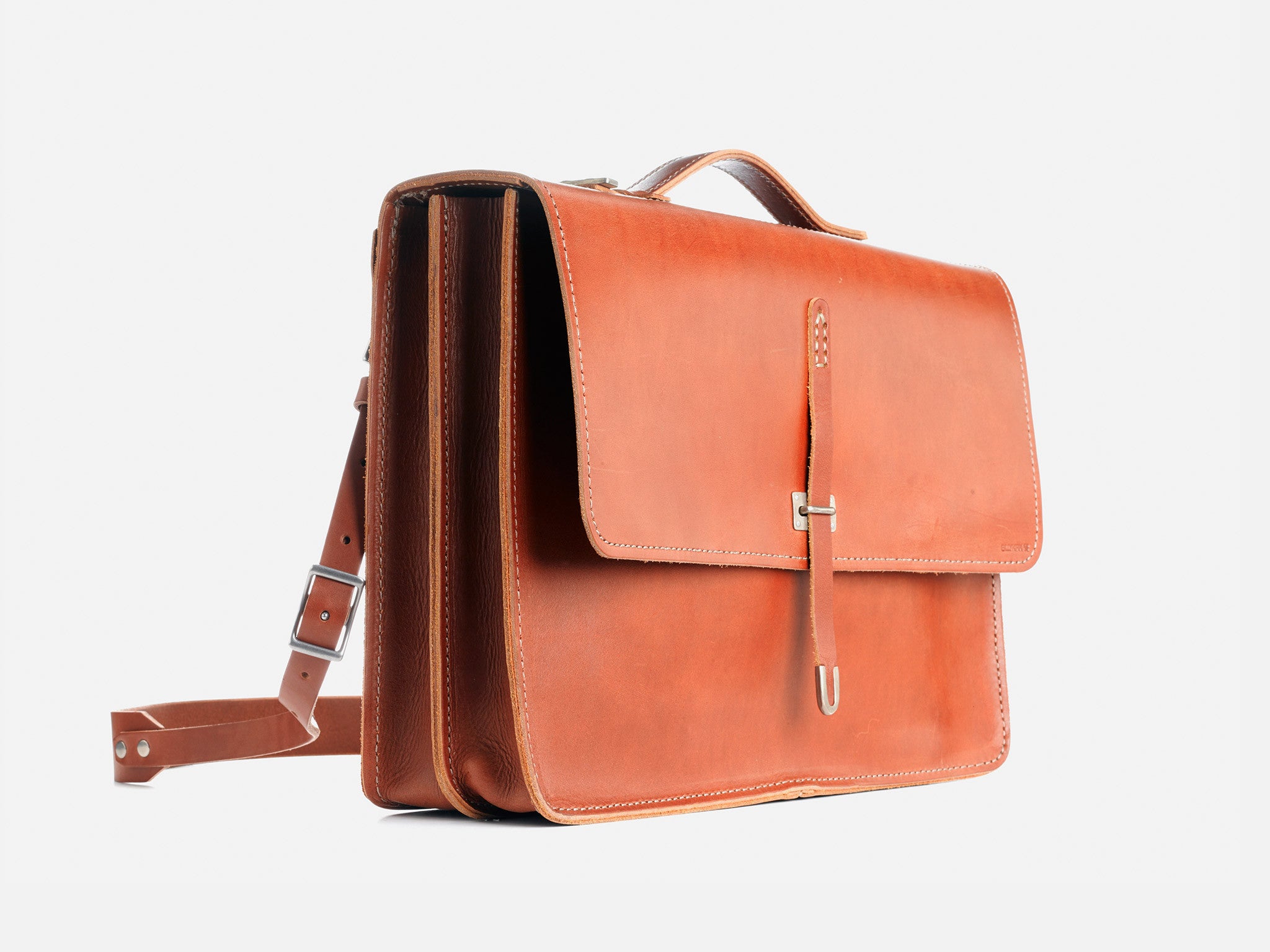 A tan leather briefcase with a top handle, front flap, buckle closure, and an adjustable shoulder strap, displayed on a white background.