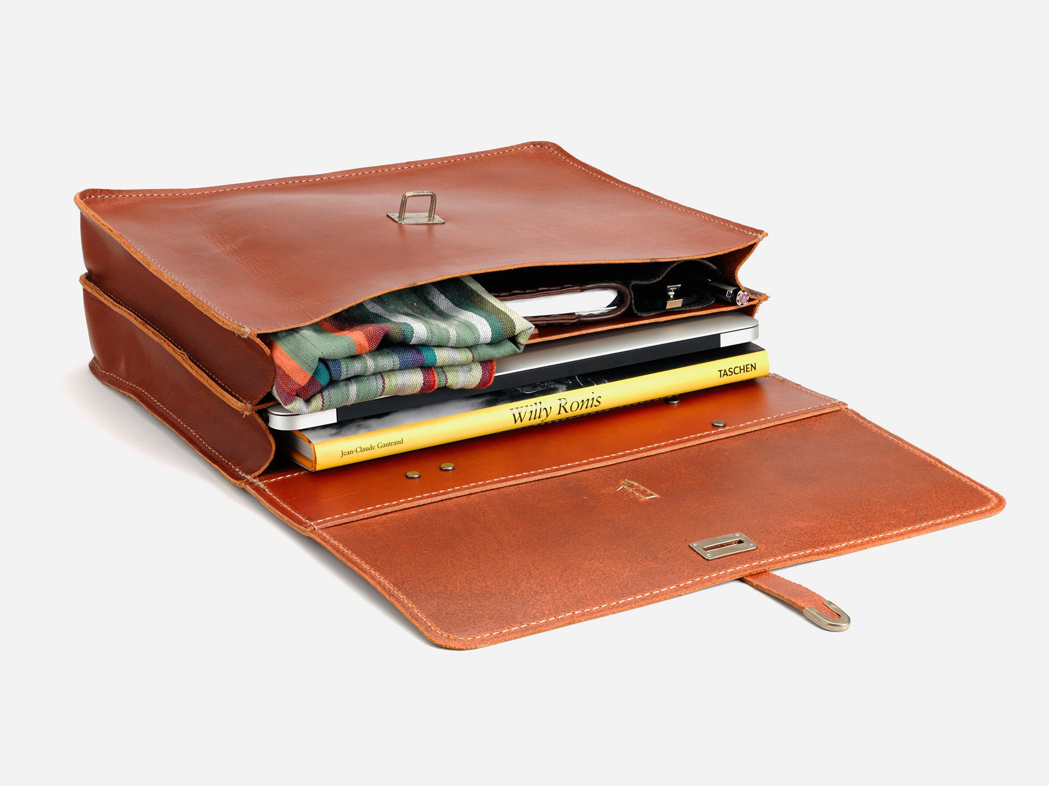 Open brown leather satchel with books, a striped cloth, a white smartphone, and other items neatly arranged inside, set against a plain white background.